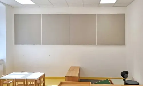 Akustikpaneele an Wand in Gruppenraum mit Tischen und Holzspielm&ouml;beln