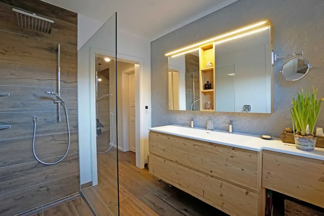 Badezimmer mit Walk-in Dusche, Holzwaschtisch und beleuchtetem Spiegel