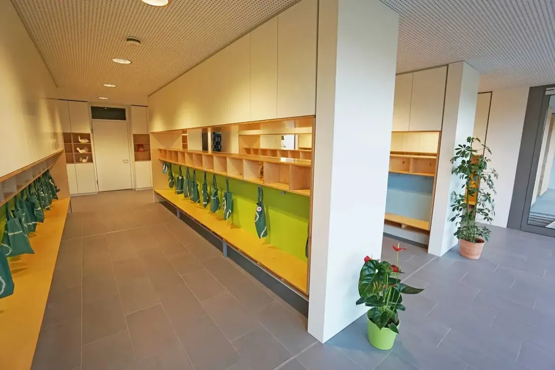 Garderobenbereich mit durchgehender Sitzbank, offenen Fächern und grünen Taschen