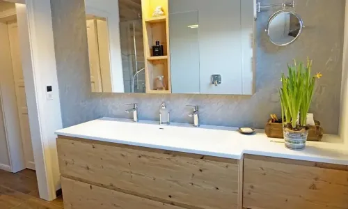 Badezimmer mit Doppelwaschbecken, Holzm&ouml;bel und beleuchtetem Spiegel